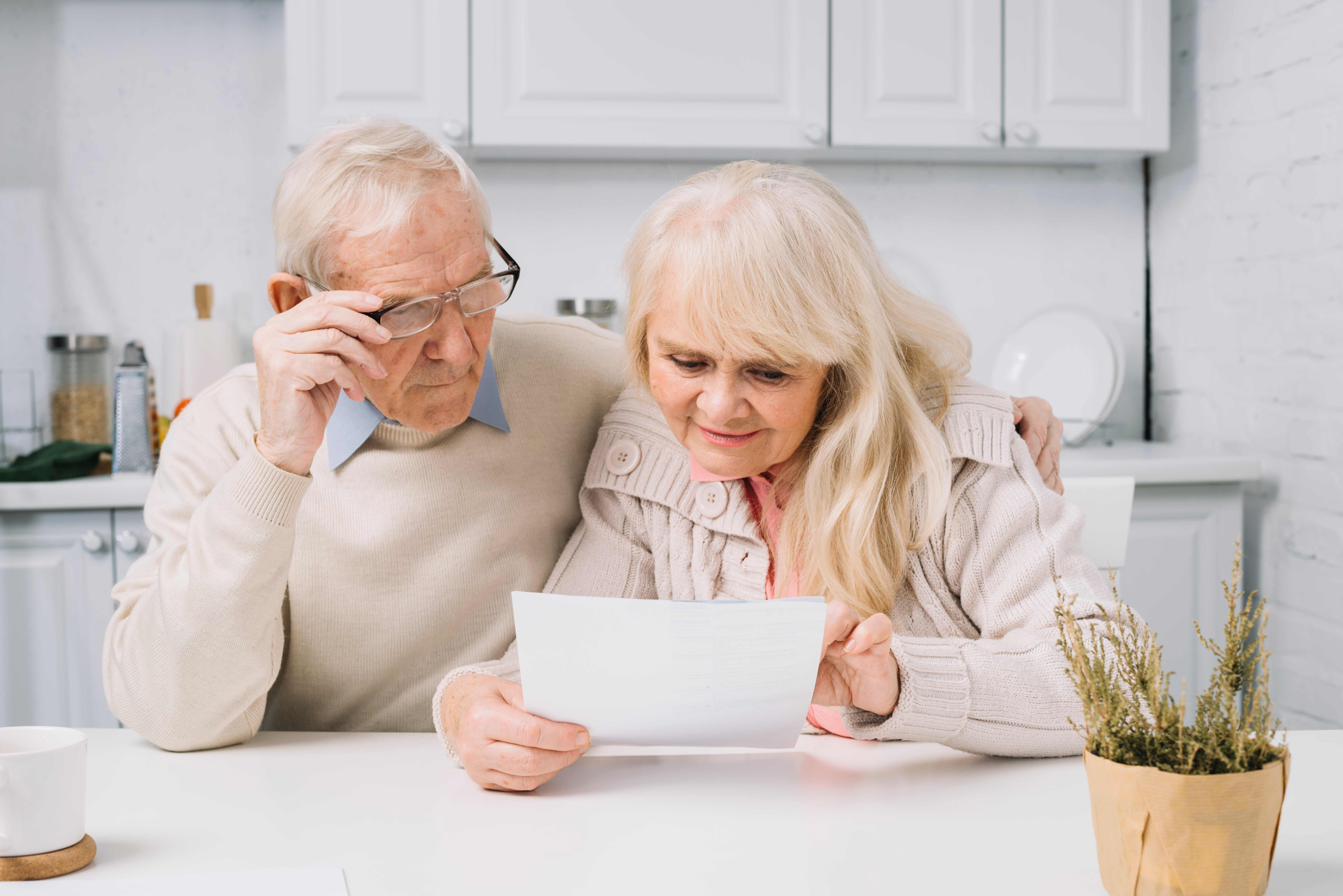 Senior couple reviewing healthcare documents and paperwork together in their kitchen, representing the challenges that SageAlly helps navigate